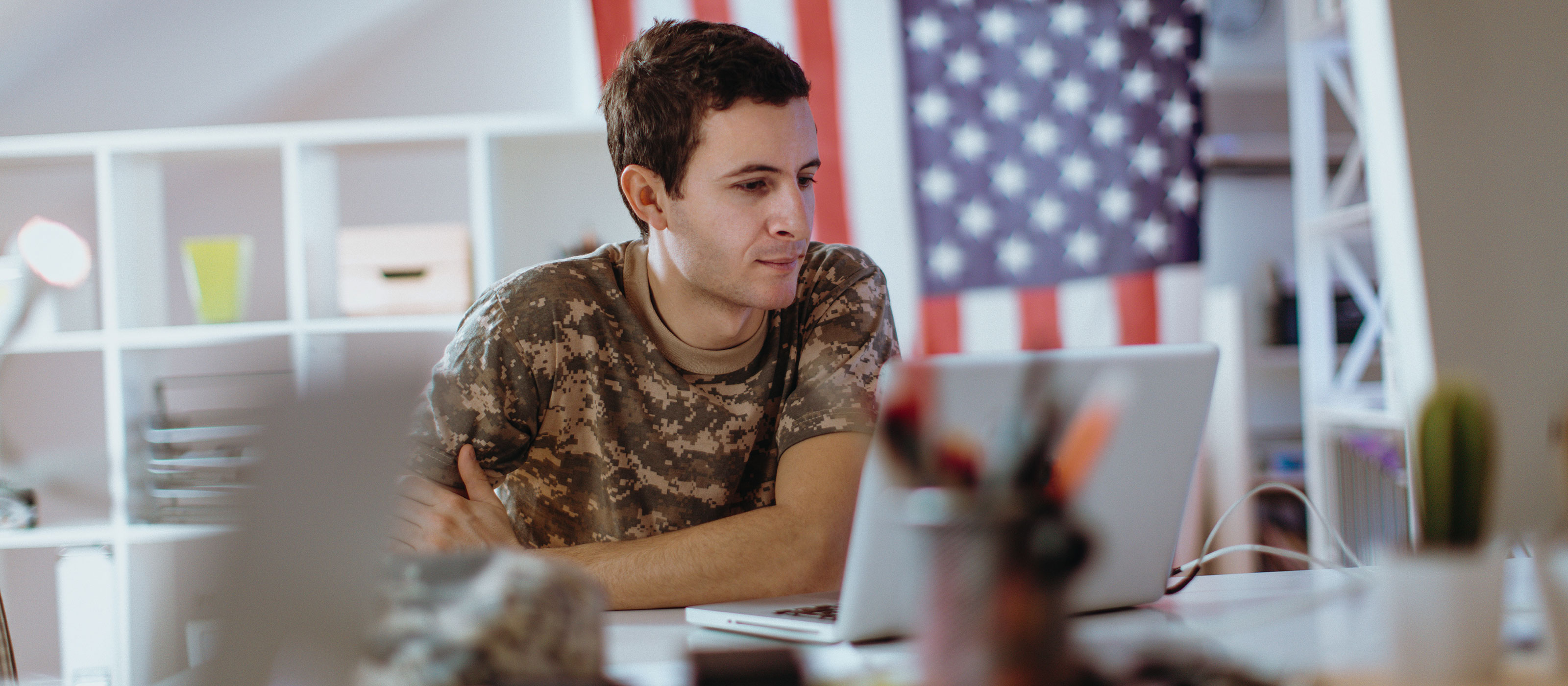 Man in camouflage sitting at a desk with a laptop