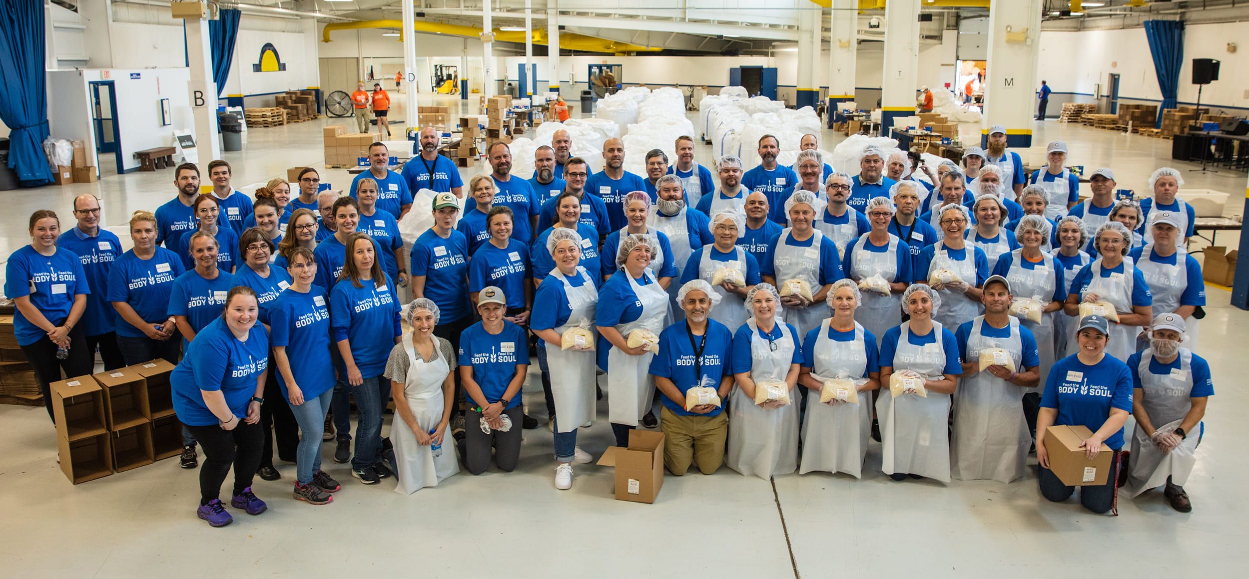 Large group of volunteers standing together at a rice packing event for a photo