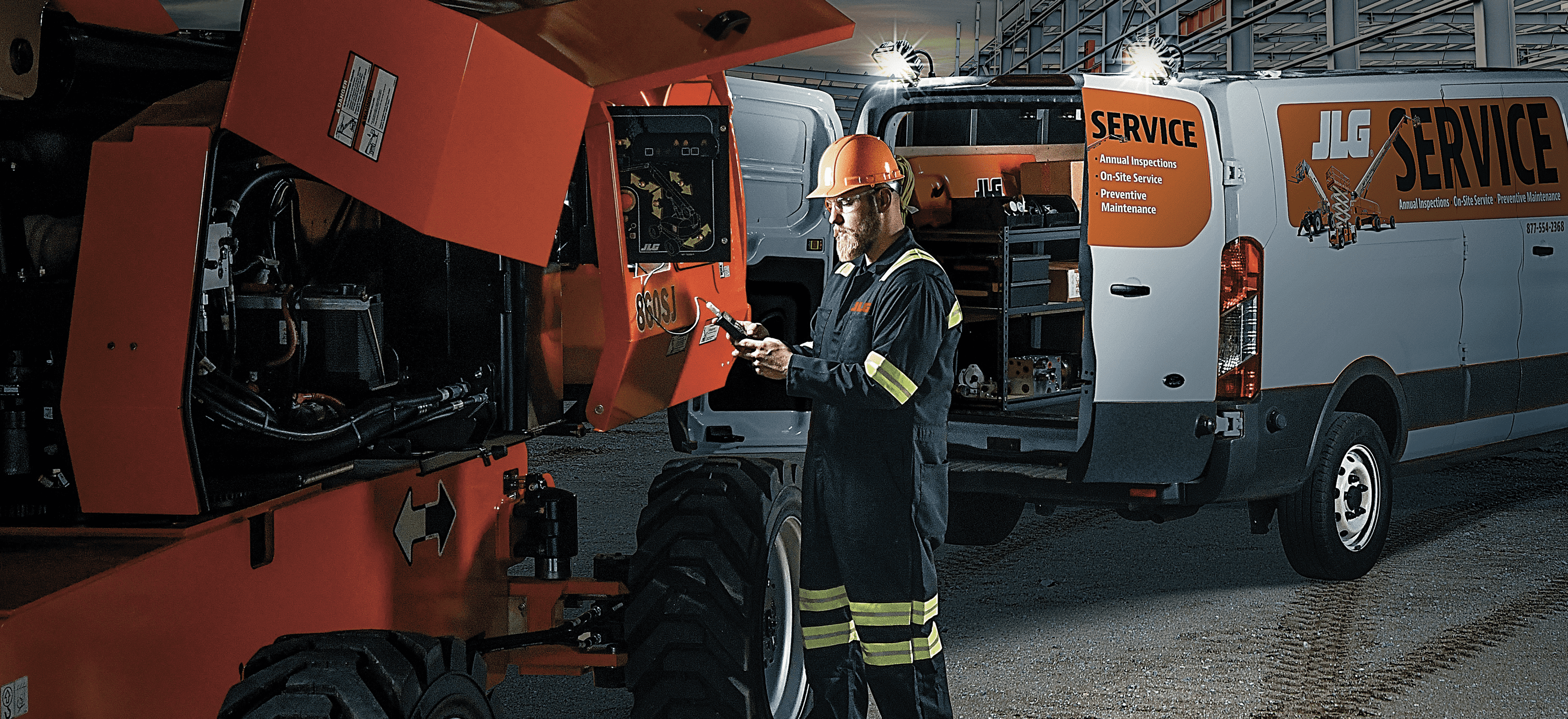 Male service technician repairing a JLG product outside at night