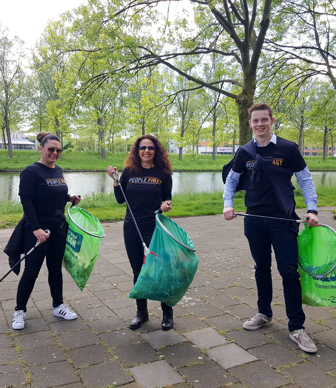 Three people holding green garbage bags and garbage pickers