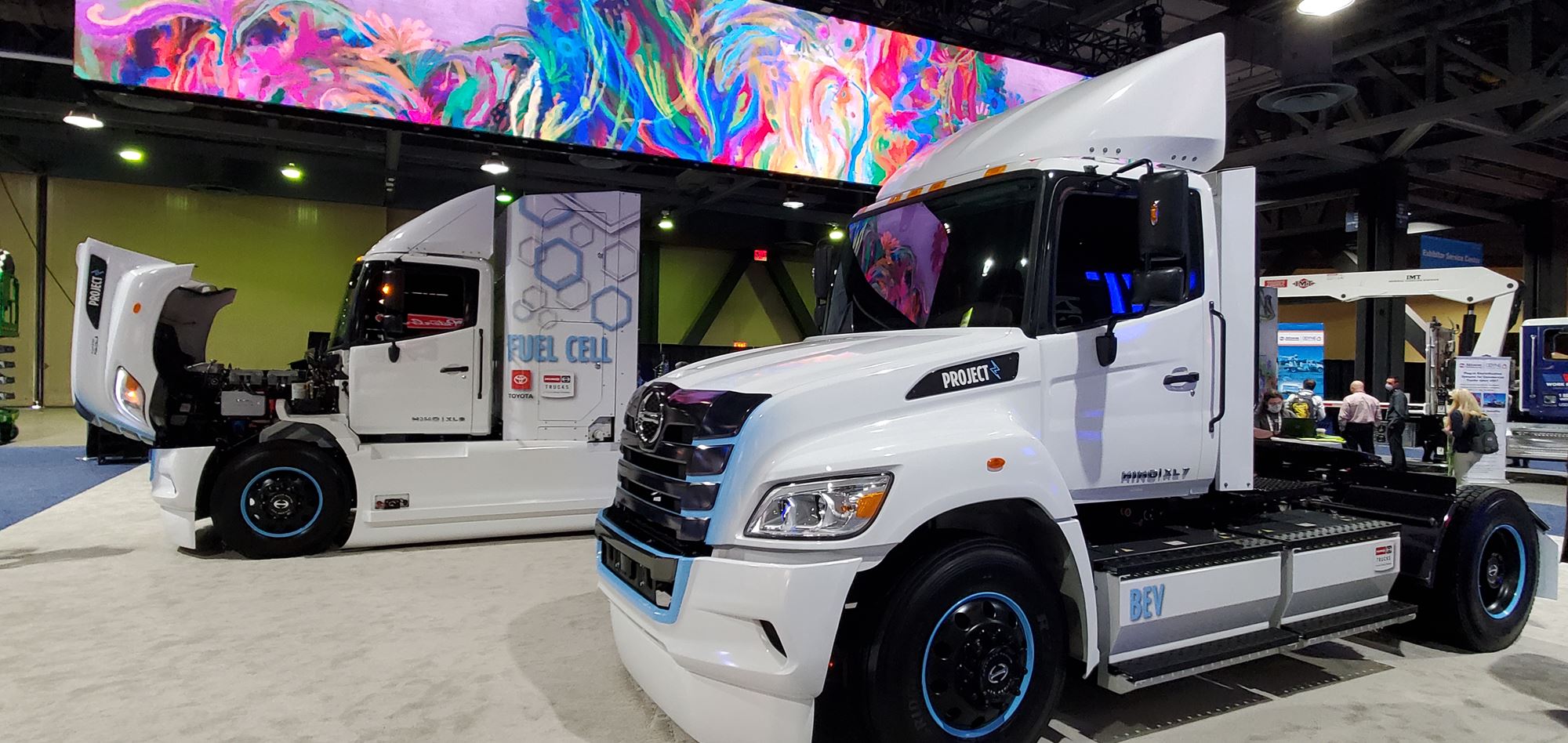 Pratt Miller zero-emission electric white semi trucks indoors at a tradeshow in partnership with Hino Motors and Toyota